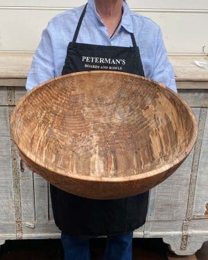 A staff member at Spencer Peterman holding a 21-inch Spalted Ambrosia Maple round bowl, showcasing striking patterns of spalting and ambrosia streaks across the golden maple surface.